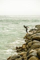 Surfer jumping into the sea from a breakwater on cloudy day