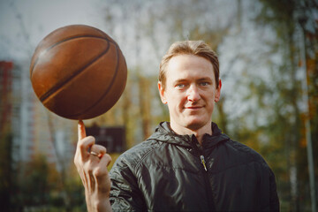 A man in a sports jacket holds a basketball on his index finger, outdoors during the day