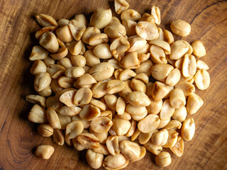 Top view of salted roasted peanuts on wooden plate, suitable for culinary content, healthy nutrition, or natural snack illustration.