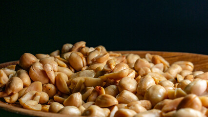 Crispy fried peanuts on a wooden plate with minimal lighting on a dark background, suitable for snack content, Eid al-Fitr, or culinary concepts.