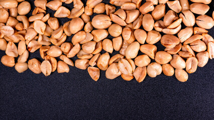 Top view of Crispy fried peanuts scattered on a black surface. Ideal for food background or creative design.