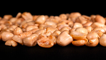 Close-up detail of crispy roasted shelled peanuts with studio lighting appearing to float on black background, perfect for healthy snack illustrations and food designs.