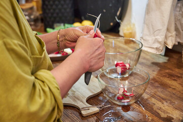 Woman slicing radishes on a wooden cutting board in the kitchen, close-up of hands