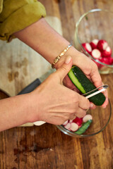 Side close-up of a woman peeling a cucumber in the kitchen to prepare a salad
