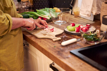 Woman slicing radishes on a wooden cutting board in the kitchen, close-up of hands