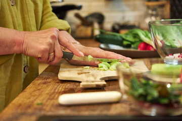 Woman slicing a cucumber on a wooden cutting board in the kitchen, close-up of hands