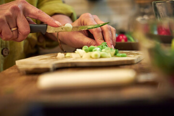 Woman chopping green onions on a wooden cutting board in the kitchen, close-up of hands