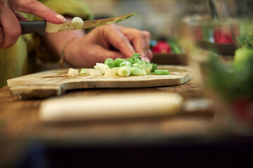 Woman chopping green onions on a wooden cutting board in the kitchen, close-up of hands