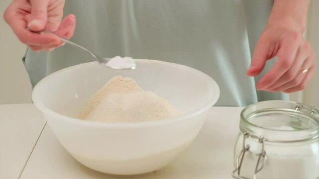 Close-up of a person adding baking soda to a bowl of flour during home baking, preparing dry ingredients for a recipe.