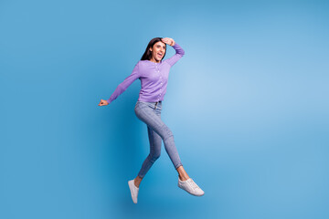 Full length view of attractive cheerful girl jumping having fun rising hands up isolated on blue color background