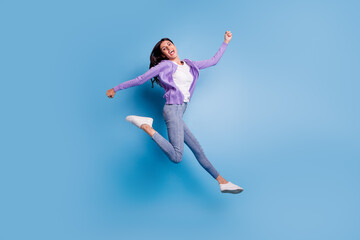 Obraz premium Full length view of attractive cheerful girl jumping having fun rising hands up isolated on blue color background
