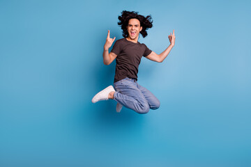 Fototapeta premium Overjoyed guy jumping and showing horns symbol over blue studio background
