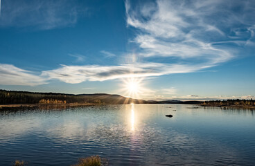 Stunning autumn sunset over a serene Scandinavian lake. Golden fall sunlight and sunbeams reflect on the tranquil water, beneath a vibrant sky and tree-lined shores