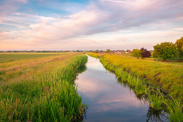 Idyllic image of a slightly winding ditch in the Dutch polder landscape under the evening sky
