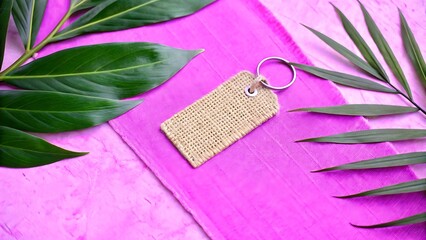 Textured burlap tag with metal ring and green leaves on a vibrant pink background