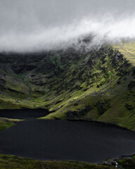 A mysterious mountain's peak is partially obscured by mist, its slopes meeting a dark, still lake. The image is evocative of solitude and grandeur.