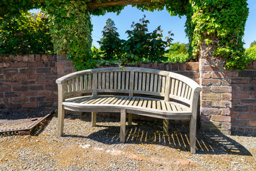 Wooden bench in a botanical garden, next to a brick wall covered with ivy. Finlaystone Country Park Estate. Scotland. UK.  