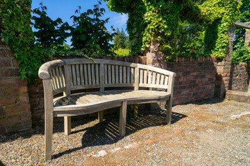 Wooden bench in a botanical garden, next to a brick wall covered with ivy. Finlaystone Country Park Estate. Scotland. UK.  