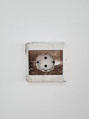 Old worn and rusty socket on white wall surface. Very dirty and rusty electrical outlets on the wall caused by dust, dirt and oxidation on the metal.