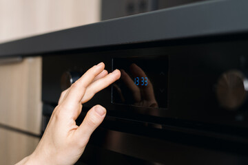 Naklejka premium Modern electric oven in a stylish kitchen with a hand adjusting the settings