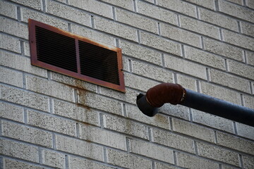 Rusted vent and water drain pipe coming out of building.