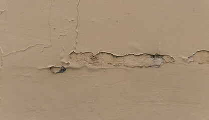 Un mur beige présente des fissures visibles et des zones de décoloration. Cette détérioration suggère un manque d'entretien sur une surface exposée aux intempéries.