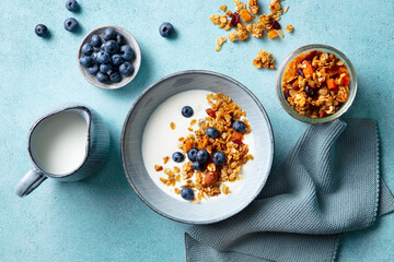 Healthy breakfast. Oat granola with fresh blueberries and milk in a bowl. Blue background. Close up. Top view.
