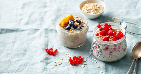 Healthy breakfast. Overnight oats with fresh berries and fruits in glass jars. Blue textile background. Close up. Copy space.