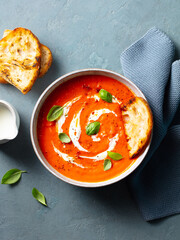 Roasted tomato soup with cream in a white bowl on grey background. Top view.