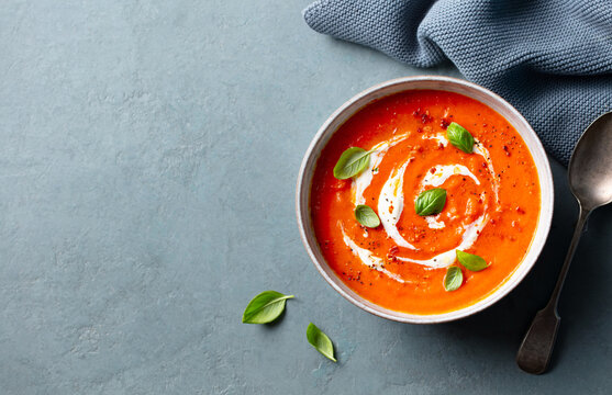 Delicious tomato cream soup in bowl on grey stone background, space for text. Top view.