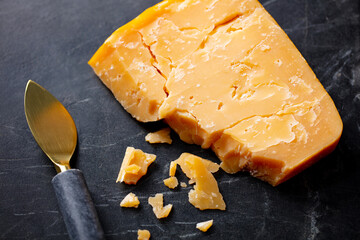 Matured cheddar cheese with knife on black marble serving board. Dark background. Close up. Top view.