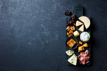 Assortment of cheese with jamon, fresh grape and nuts on marble cutting board. Dark grey background. Copy space. Top view.