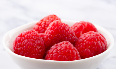Fresh raspberries in a white bowl. light background. Close up.