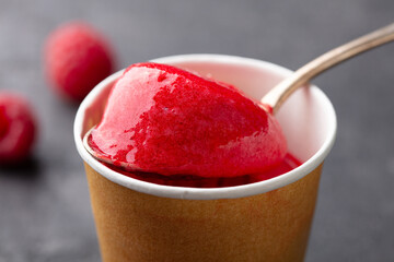 Red sorbet ice cream in an outdoor paper cup. Grey background. Close up.