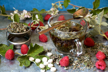Himbeerblättertee in einer glastasse mit Himbeeren, Blüten und Tabletten
