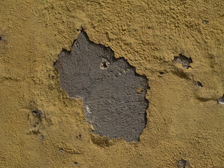 Close-up of cracked yellow wall plaster revealing the underlying gray concrete structure. Weathered, rough texture suitable for backgrounds and design