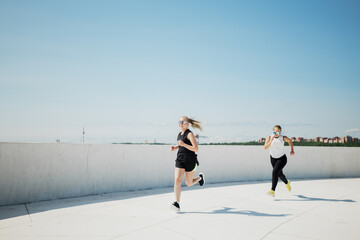 Two women enjoy an energetic run together along a scenic waterfront path under a bright blue sky