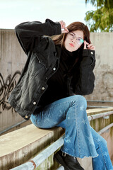 Thoughtful Young Woman Framing Glasses in Urban Setting
