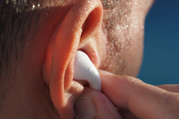 Close-up of a person inserting wet waterproof earbud into ear in swimming pool. Selective focus. 