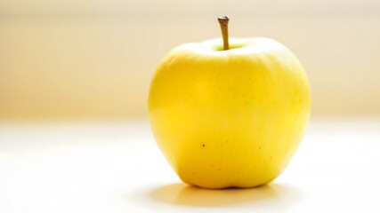 A bright yellow apple sits on a white table
