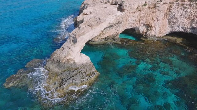 Smooth flyover of the Love Arch in Ayia Napa, Cyprus, showcasing the natural rock formation, turquoise waters, and gentle waves along the coast.