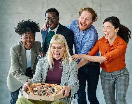 Portrait of young businesspeople, businessman and businesswoman or students having fun during a meeting or a break eating pizza in the office.