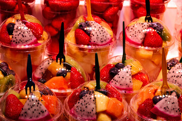 cups of colorful sliced fruits. transparent clear plastic cups with caps and fork. street vendor...
