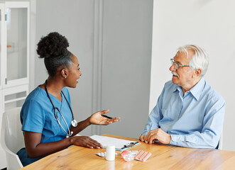 Doctor or nurse caregiver showing a prescrption or documents and holding drug bottle to senior man at home or nursing home