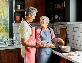 Portrait of happy senior mid aged mature couple prepering meal with fresh vegatebles in kitchen at...