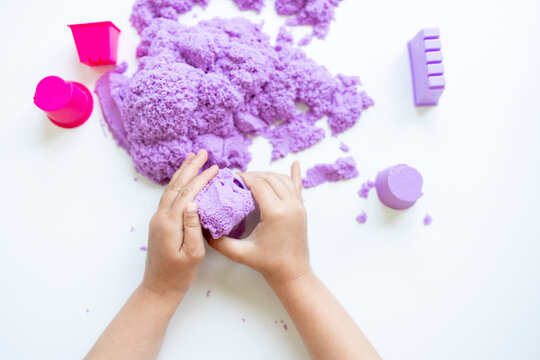 Child hands playing with purple kinetic sand on white surface