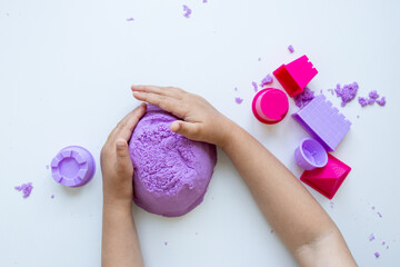 Child hands molding purple kinetic sand with colorful molds on white background