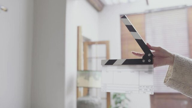 A hand holding a movie clapperboard, ready for filming. The clapperboard is black and white, and the background is blurry.