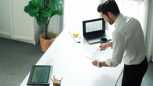 Architect engineer using laptop planning house design at office while sitting at meeting table with blueprint and equipment scatter around.Skilled civil engineer working at blueprint. Alimentation.