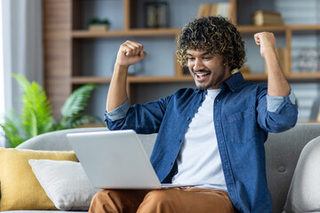 A young man celebrates a success while looking at his laptop, expressing happiness and excitement.